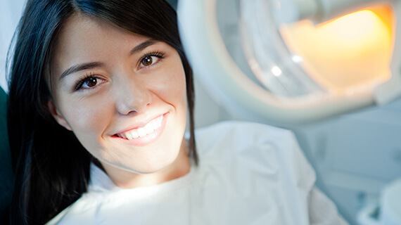 A Woman Smiling Under a Light for Dental Treatment