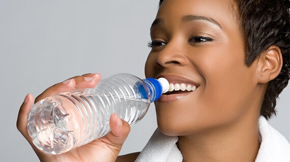 A woman smiling and about to drink water from a bottle.